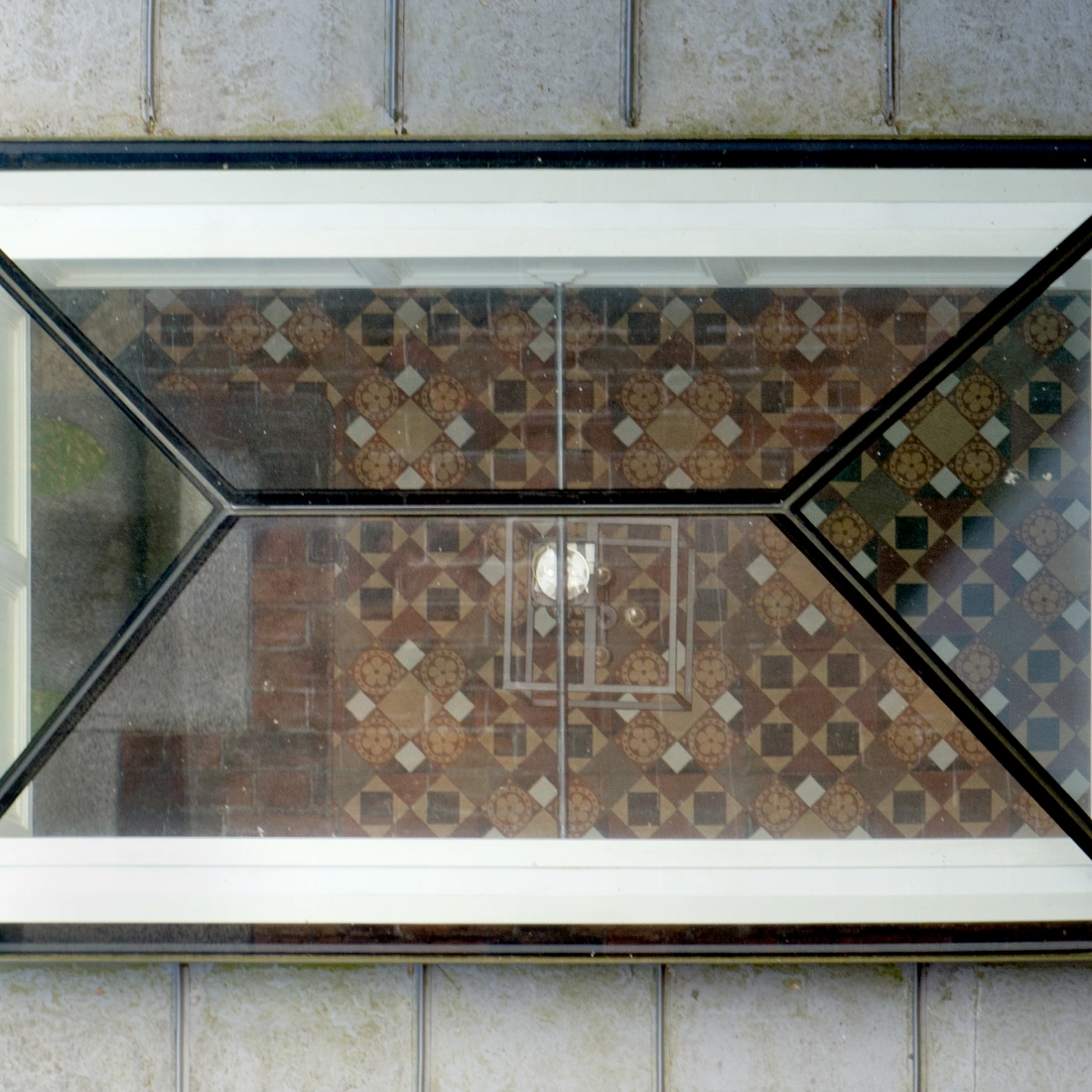 Vitrage rectangulaire, avec des coins en métal noir, montrant un sol en mosaïque de carreaux colorés en dessous.