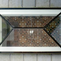 A geometric window framed in black, reflecting a patterned tiled floor with intricate designs in various colors. Natural light illuminates the space visible through the window.