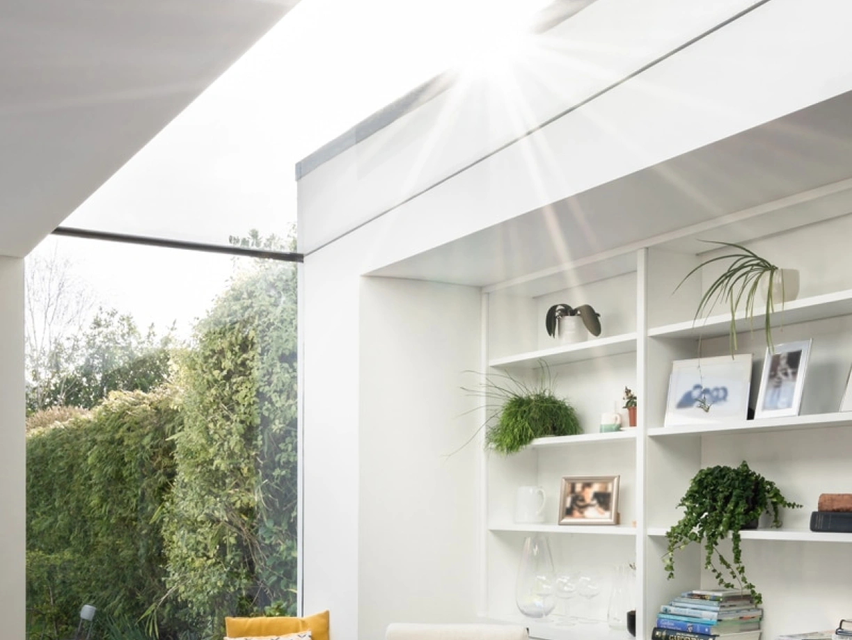 Luminose salone con una grande finestra cupolata, un mobilio elegante, e una vista di un giardino verde. Una sedia comoda è posizionata vicino a una libreria bianca, adornata con piante e decorazioni.