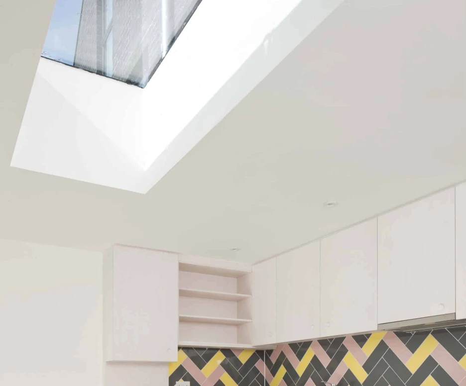 A modern kitchen featuring white cabinets, a colorful herringbone-patterned backsplash in shades of pink, yellow, and gray, and a skylight that lets in natural light.
