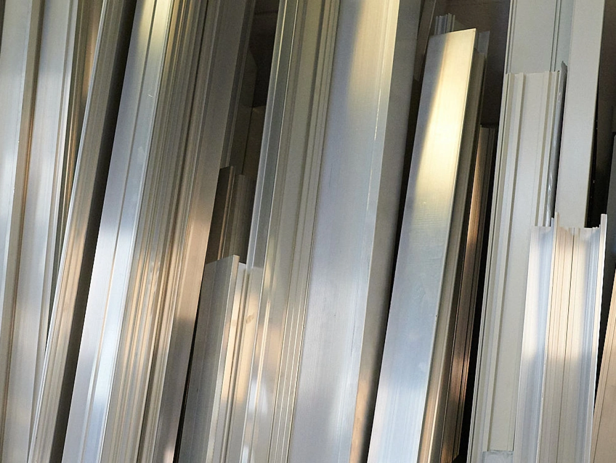 A collection of shiny, metallic aluminum strips and extrusions stacked closely together, reflecting light.