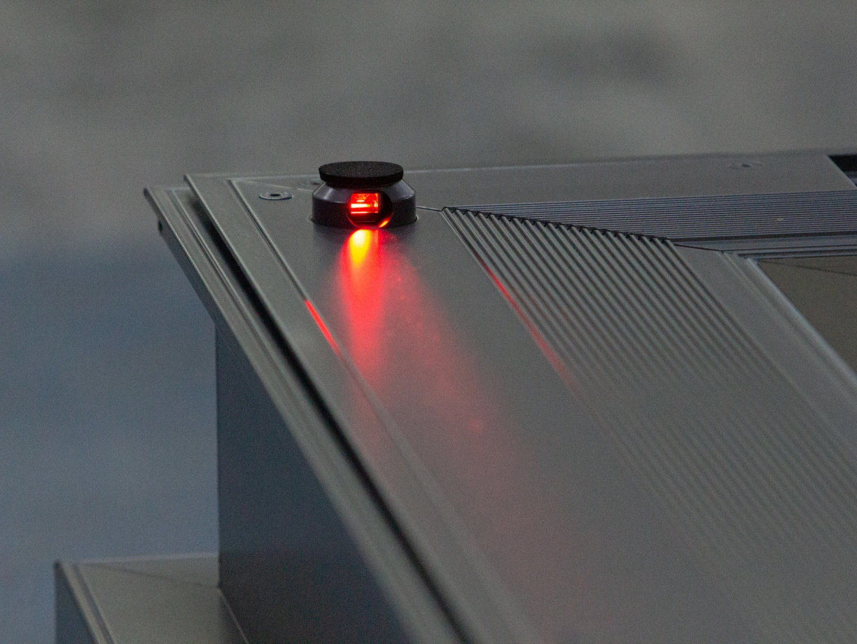 Botón en un dispositivo electrónico con luz roja encendida. La superficie es gris y texturizada.