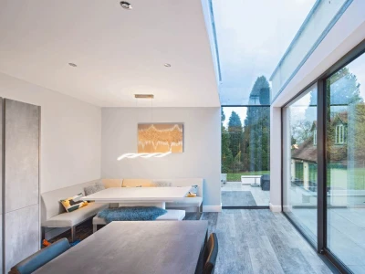 Interior moderno con comedor minimalista y grandes ventanales que ofrecen vista a un jardín. La luz natural ilumina el espacio, que presenta una paleta de colores neutros.