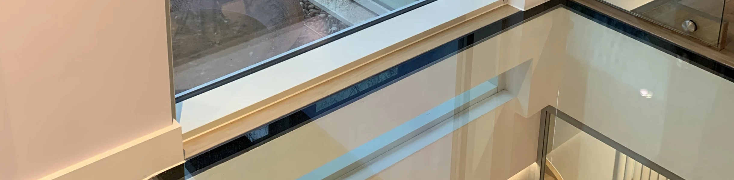 Ventana grande con un marco moderno, mostrando el exterior de una casa y el reflejo de una persona. El área interior cuenta con un piso de baldosas y una escalera de vidrio.
