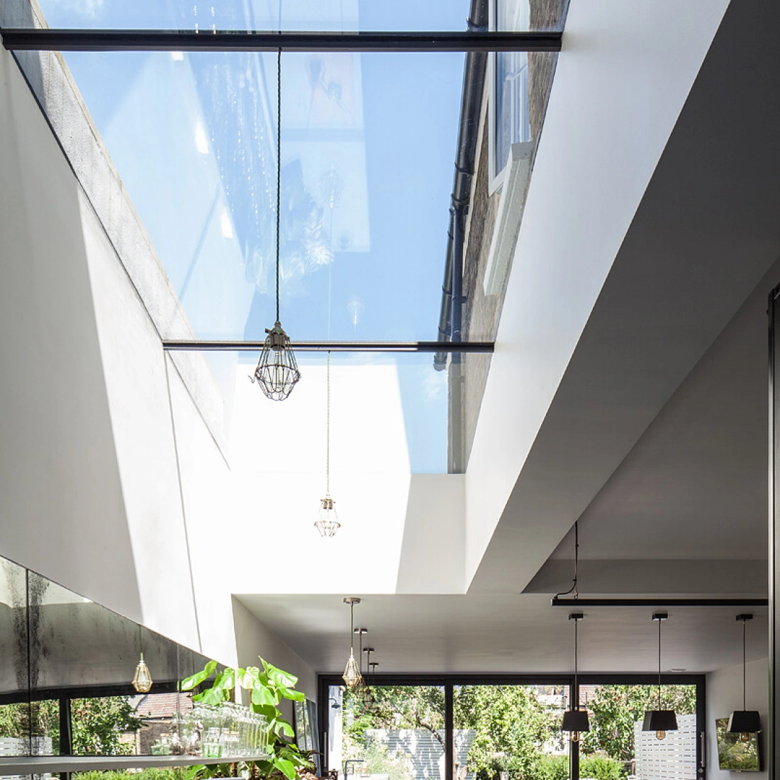 Cuisine moderne avec un design épuré, dotée de murs blancs, de comptoirs en béton et de grandes fenêtres laissant passer la lumière naturelle. Un éclairage suspendu et des plantes ajoutent une touche de verdure.