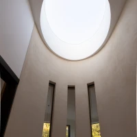 Espacio interior con paredes de color claro y ventanas verticales. Un tragaluz circular en el techo permite la entrada de luz natural, iluminando el ambiente.