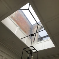 Ventana de tejado rectangular con marco negro, iluminando una habitación con un elegante candelabro de diseño minimalista.