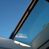 Vue d'un ciel bleu à travers un vitrage de toiture, avec des lignes géométriques créées par les bords du cadre.