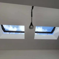 Two square skylights in a white ceiling, revealing a bright blue sky with clouds above. A light fixture hangs below one of the skylights.