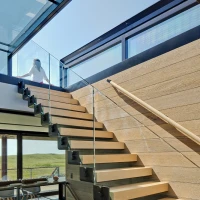 A modern staircase with wooden steps and glass railing, leading to a bright upper floor. Natural light floods the space, highlighting the contemporary design.