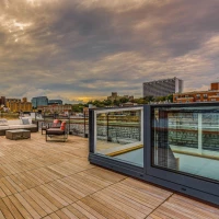 Terrasse spacieuse avec des meubles modernes, vue sur un paysage urbain et un ciel nuageux. Des bâtiments se profilent à l'horizon.